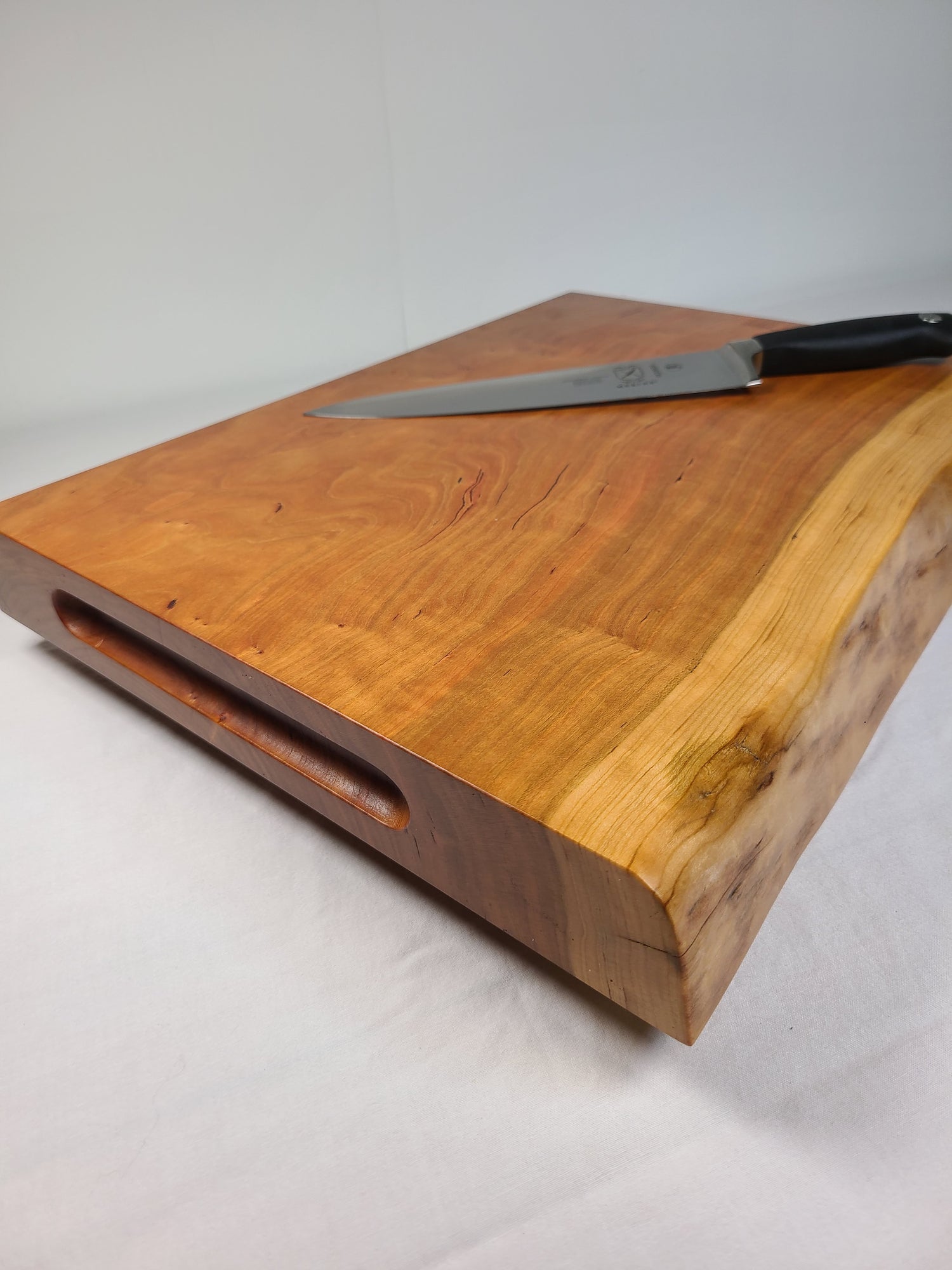 side view of a thick cherry live edge cutting board with routed handles