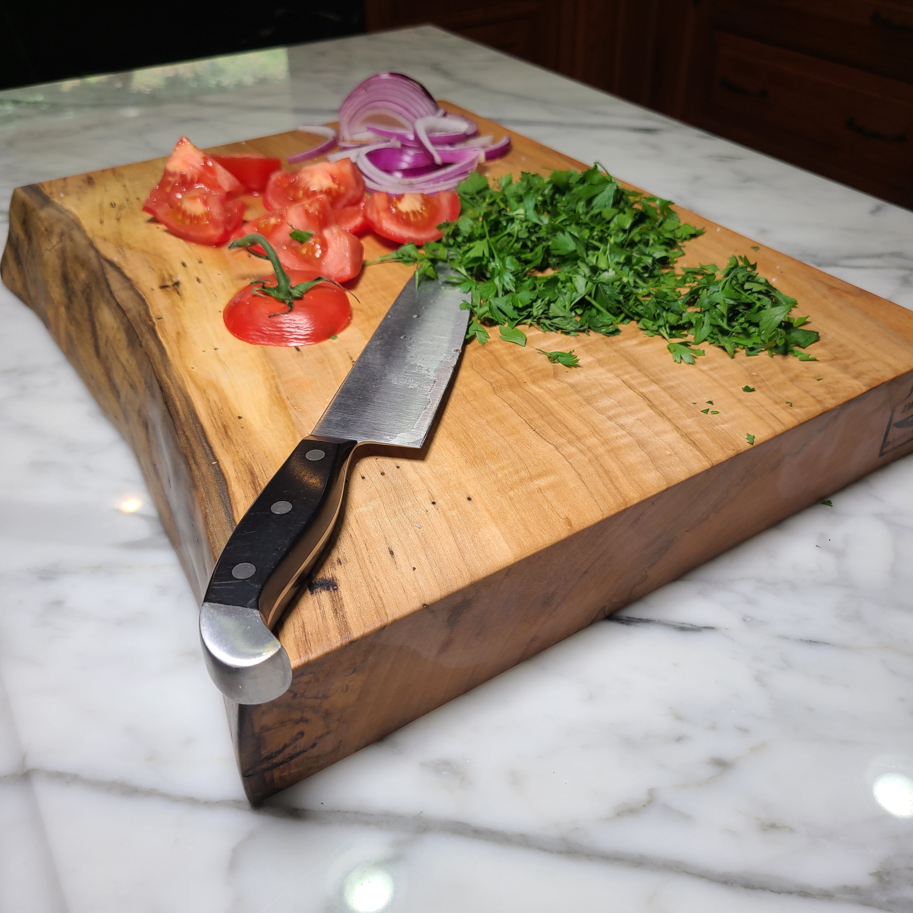 Wooden cutting board with knife, tomatoes, and herbs on a marble surface