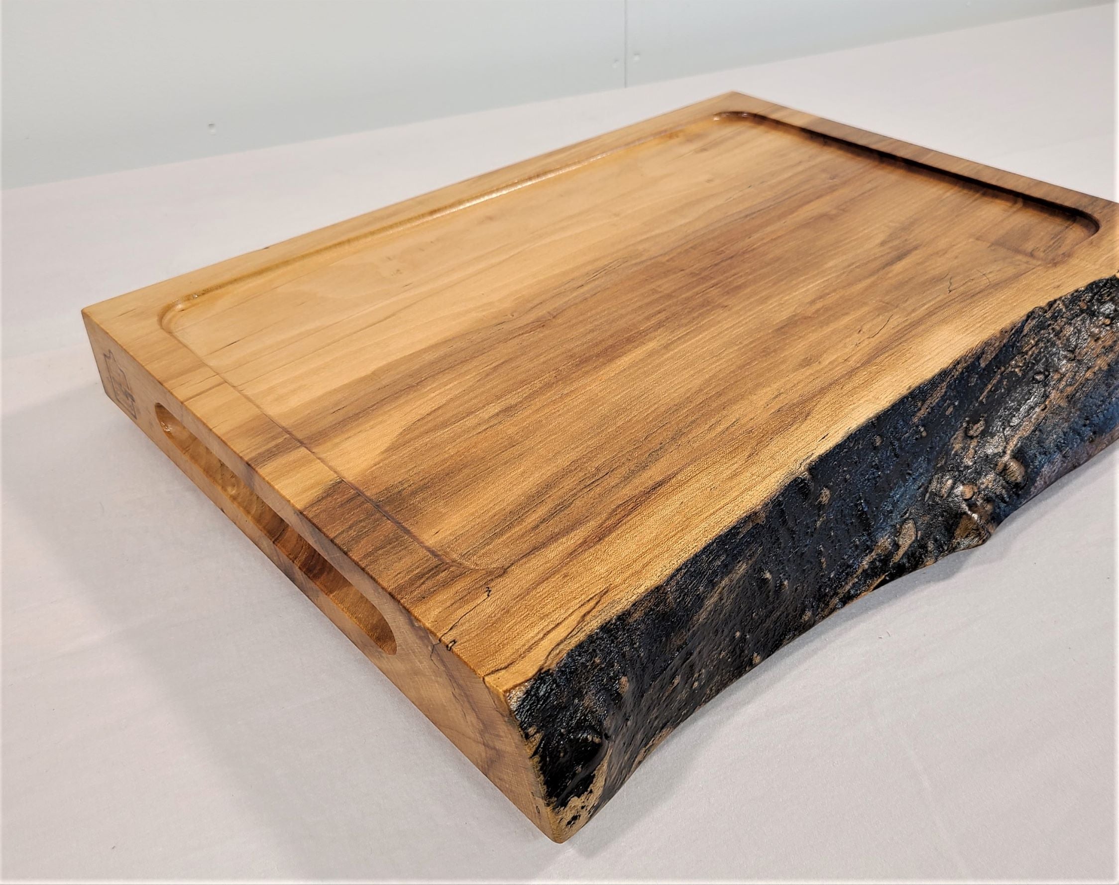 Large Thick  maple cutting board with a live edge.  Features a scooped out center area to accommodate drippings from large  meat and poultry.  Routed out handholds  for easy handling.  Reverses to solid surface cutting board.  Custom made in USA by Zimboards