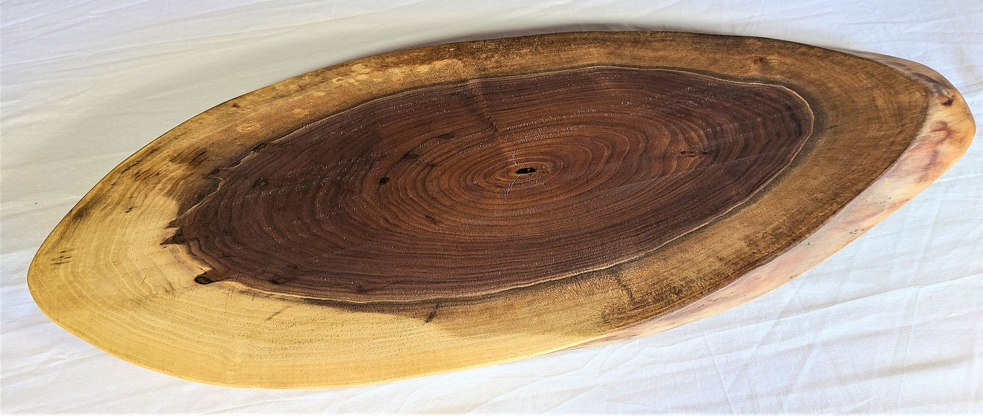 Wood charcuterie board made of walnut with a unique oval shape.  Beautiful depth of color and  live edge will make  what ever you serve look great.  Made in USA 
