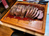 Carving board made of 2" thick cherry with a sliced prime rib with all juices caught in the well, instead of just a drip ring found in the typical carving board.  This custom cutting board reverses to a flat top and becomes a live edge charcuterie board.  Made in USA by ZimBoards.