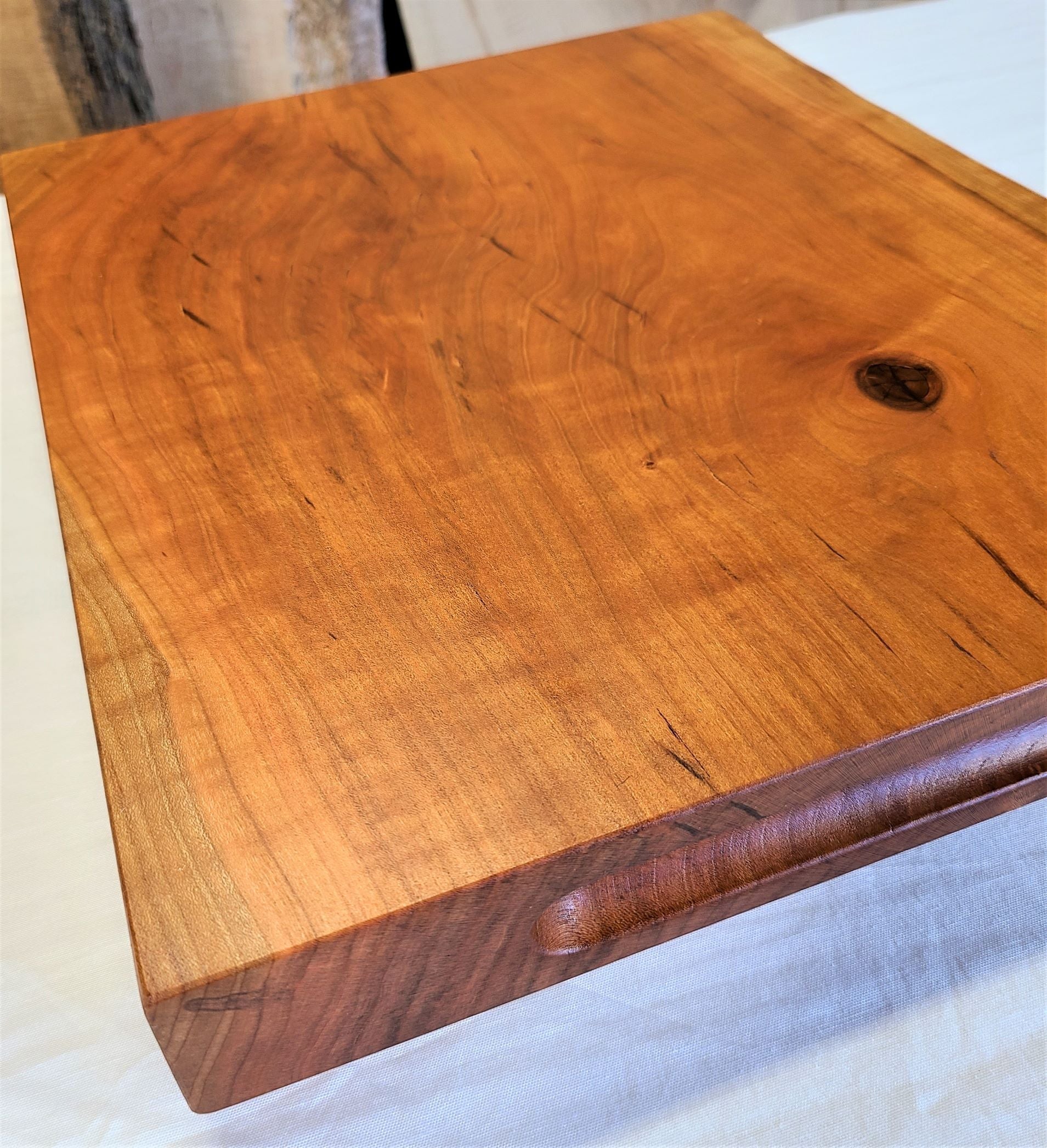 2" thick cherry custom cutting board.  Flat surface on both sides and has a live edge and routed finger holds.  Made in USA by ZimBoards.