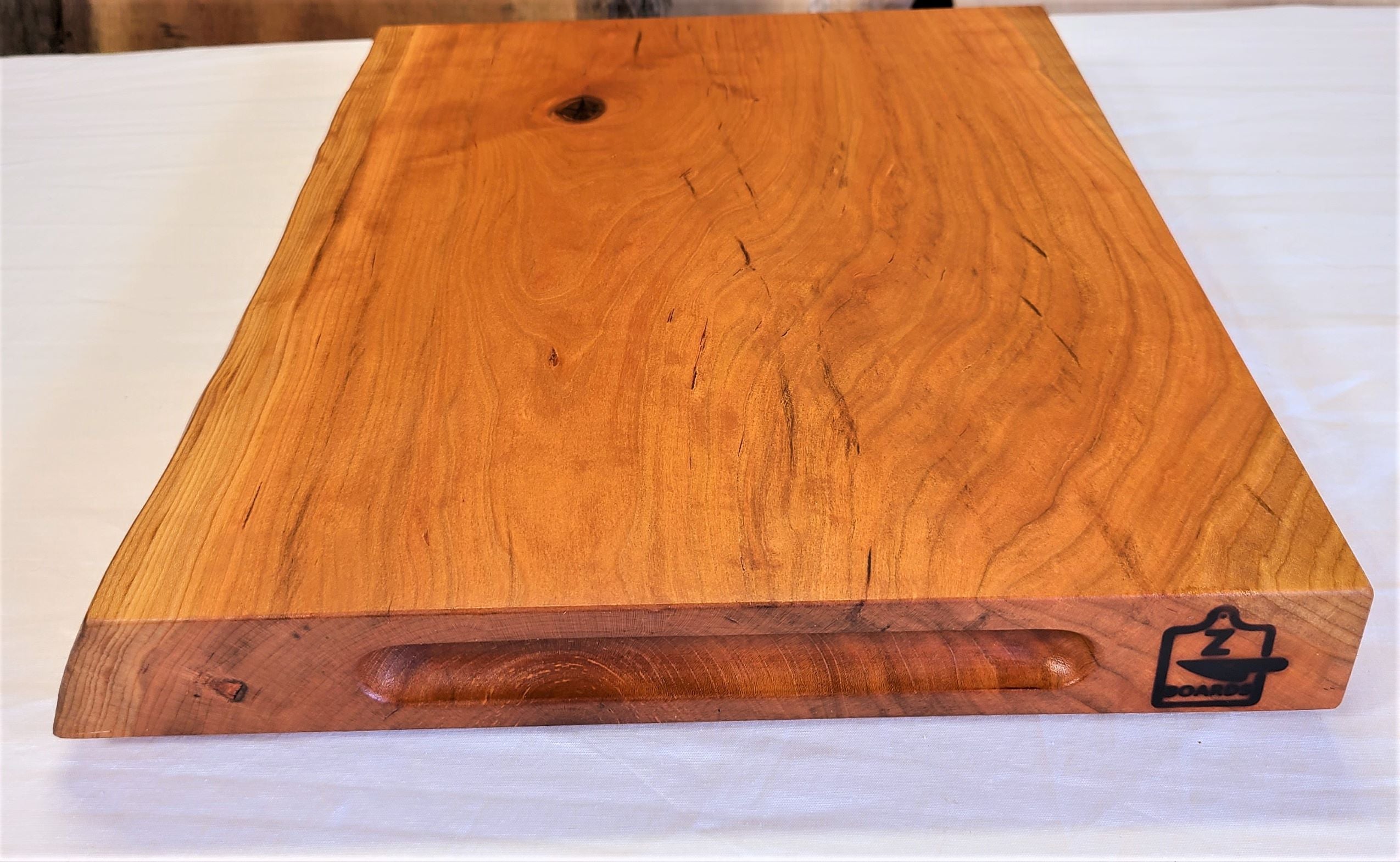 Side view of a 2" thick high end custom cutting board made of cherry.  Features a live edge and routed finger holds.  Made in USA by ZimBoards