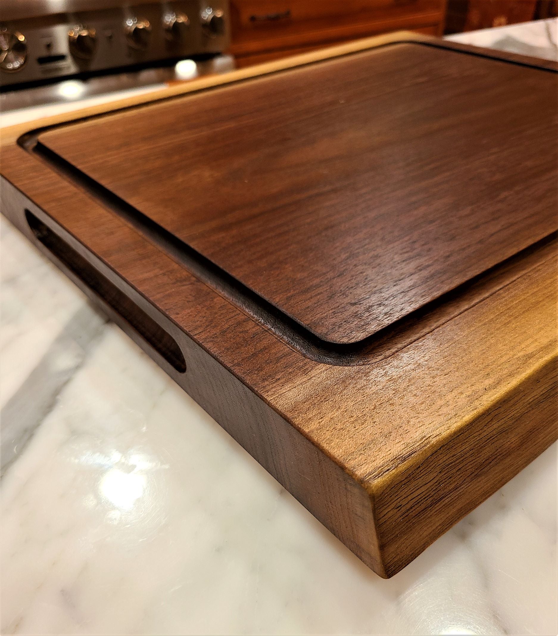 Artistic view of a walnut cutting board featuring the 2 inch thickness deep oversize juice groove and routed handhold.  Made by ZimBoards in the USA